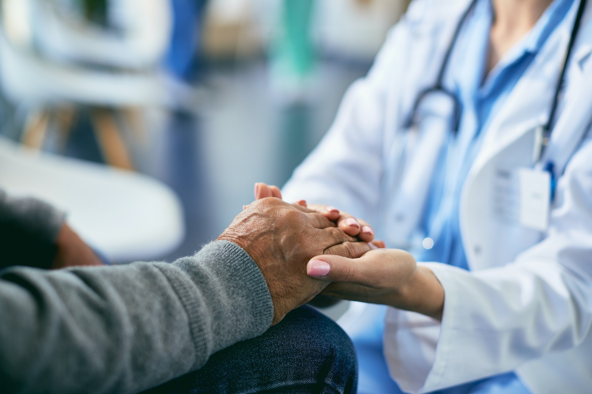 Close-up of attentive female doctor holding hands of her senior patient at medical clinic.