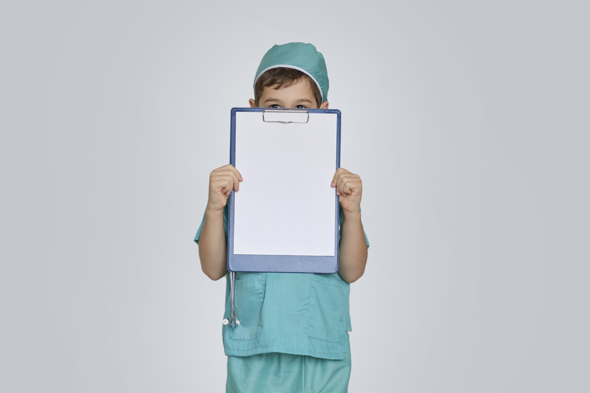 funny boy in medical uniform peeking out from behind clipboard. medical examination. Pediatrics